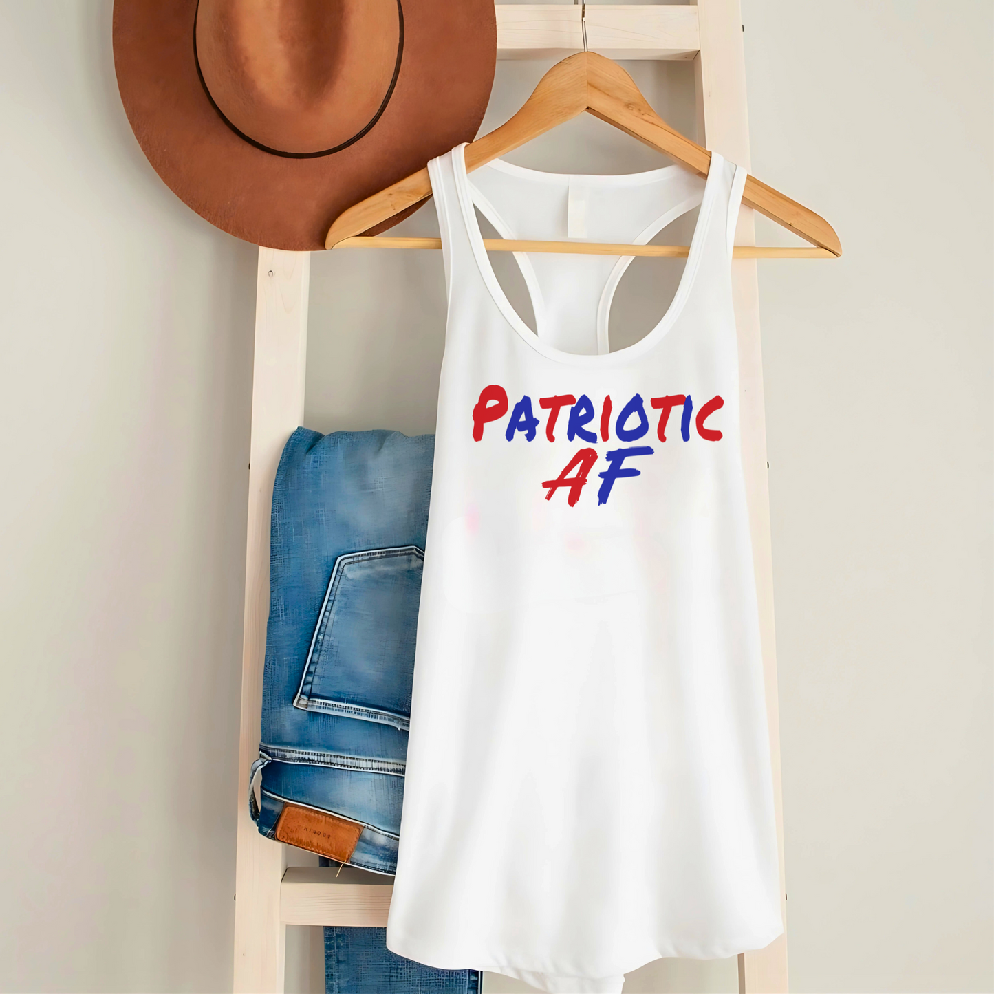 White racerback tank top on hanger with jeans and hat, "Patriotic AF" patriotic design.
