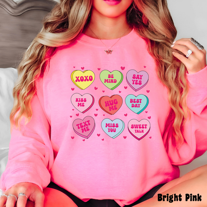 Woman wearing a Bright Pink Valentine’s sweatshirt featuring colorful candy conversation hearts with messages like “XOXO,” “Be Mine,” “Say Yes,” “Kiss Me,” “Hug Me,” and more.