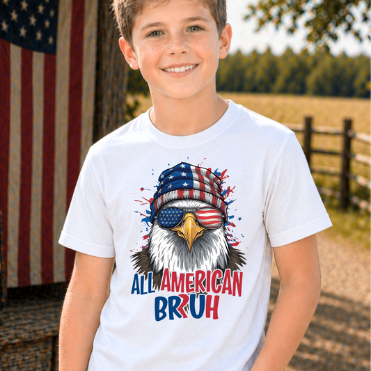 Child wearing a t-shirt with an eagle graphic and 'All American Bruh' text, standing outdoors.