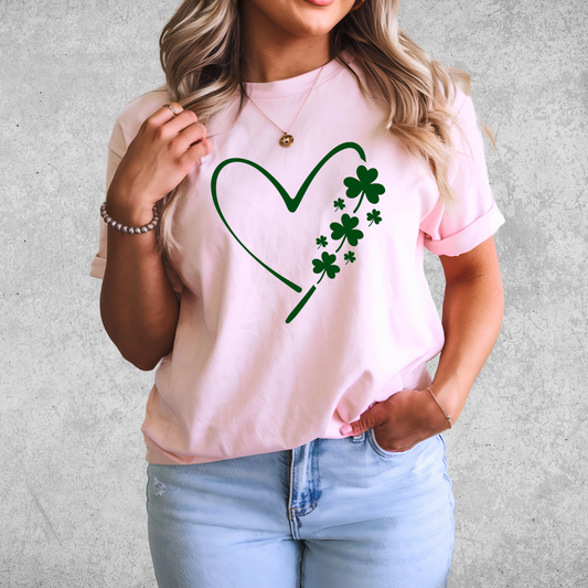 A woman wearing a pink T-shirt with a minimalist green heart and shamrock design, perfect for St. Patrick’s Day celebrations.
