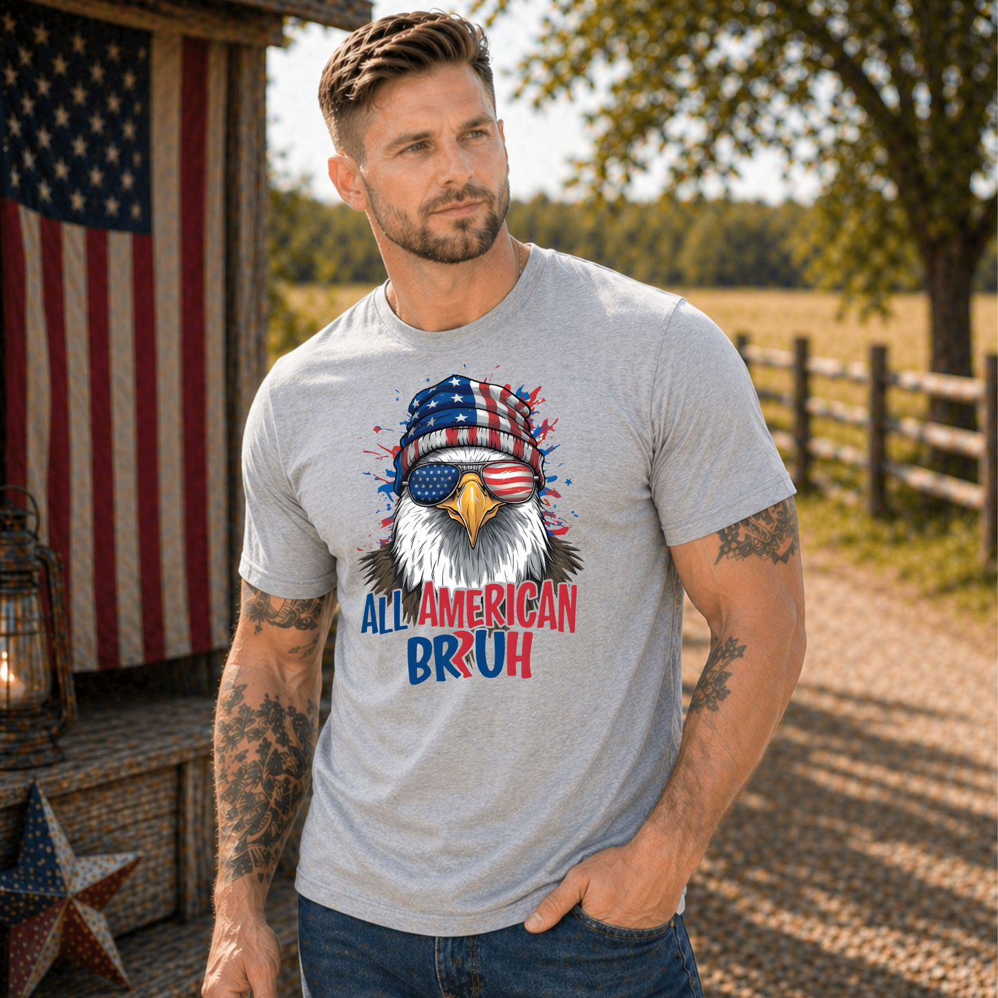 Man wearing a t-shirt with an eagle graphic and text, standing outdoors with American flag and barn in background.