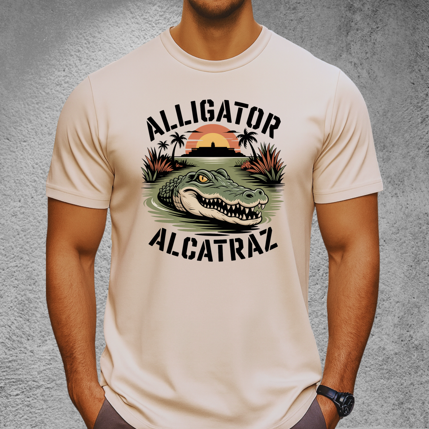 Athletic man wearing a sand-colored Alligator Alcatraz T-shirt. Graphic includes an aggressive alligator in marsh water with a distant sunset over Alcatraz. Perfect rugged men’s shirt for outdoor lovers and vacation style.

