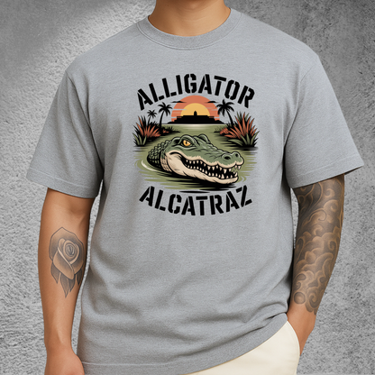 Model wearing a light gray Alligator Alcatraz T-shirt with a fierce gator graphic, Alcatraz silhouette, and sunset background. Unisex men's tee perfect for travelers, nature lovers, and graphic shirt collectors.