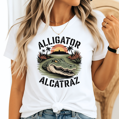 Blonde woman wearing a white Alligator Alcatraz T-shirt with a colorful alligator and prison sunset graphic. Stylish knotted tee in a relaxed unisex fit for women.