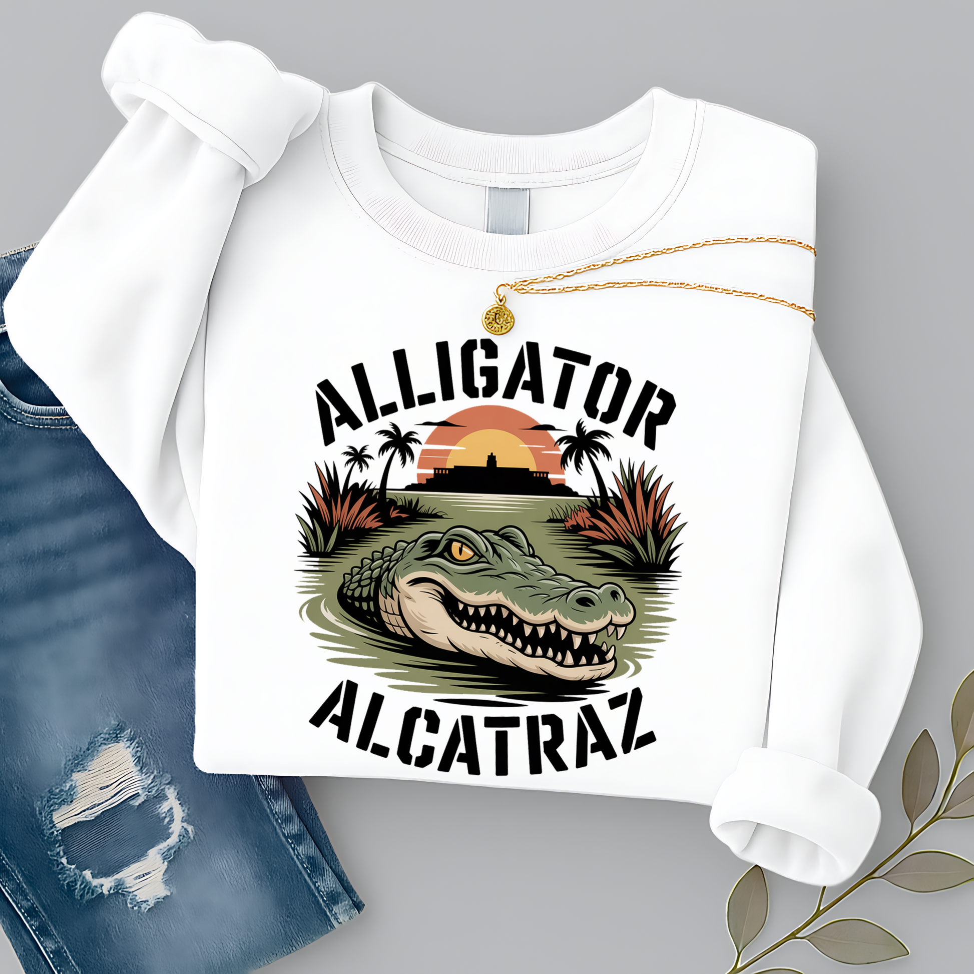 Women’s white Alligator Alcatraz sweatshirt, vintage wildlife graphic with tropical sunset and alligator design, styled flat lay with jeans and gold necklace