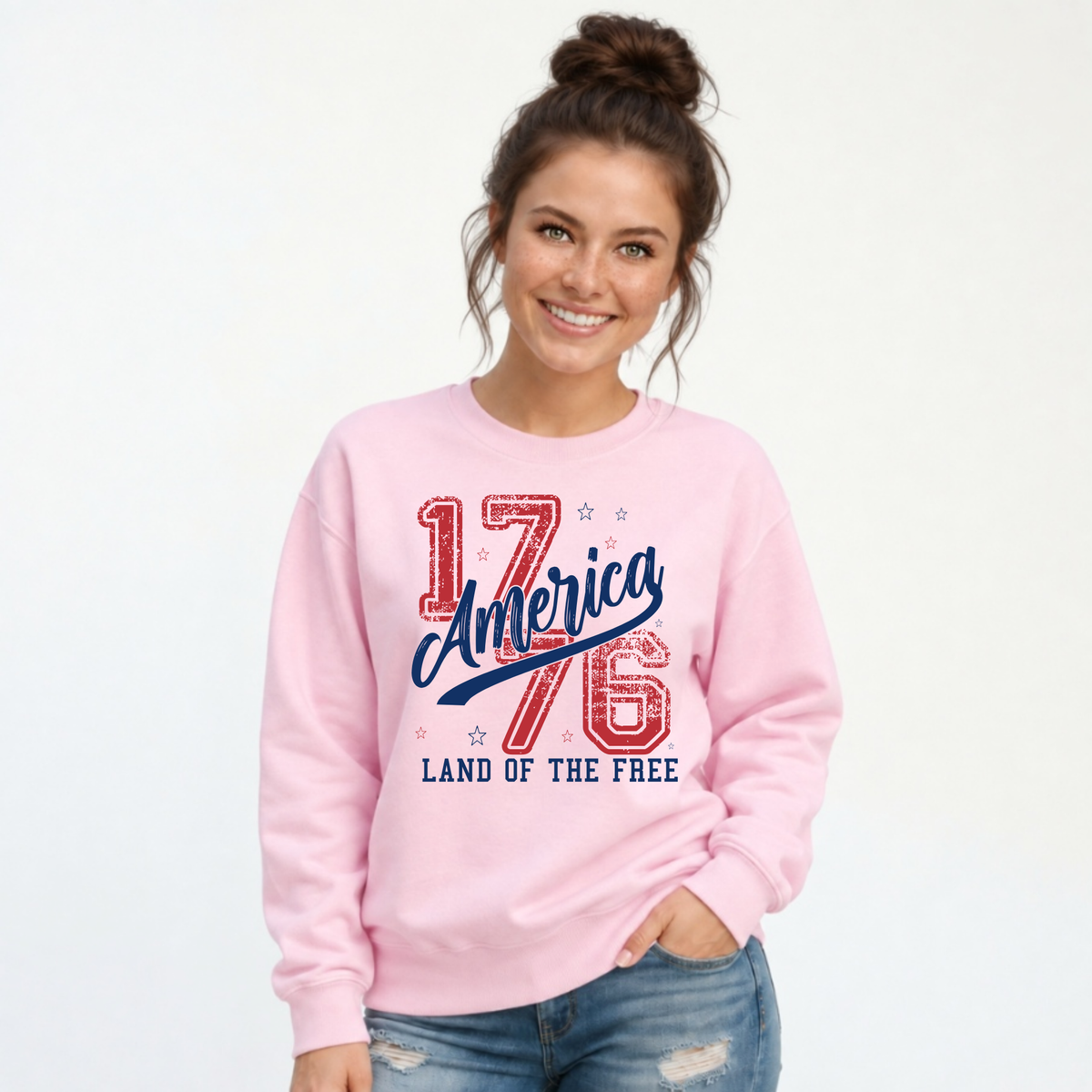 Woman wearing a light pink crewneck sweatshirt with a distressed red and blue America 1776 Land of the Free graphic