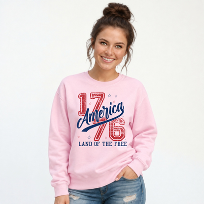 Woman wearing a light pink crewneck sweatshirt with a distressed red and blue America 1776 Land of the Free graphic