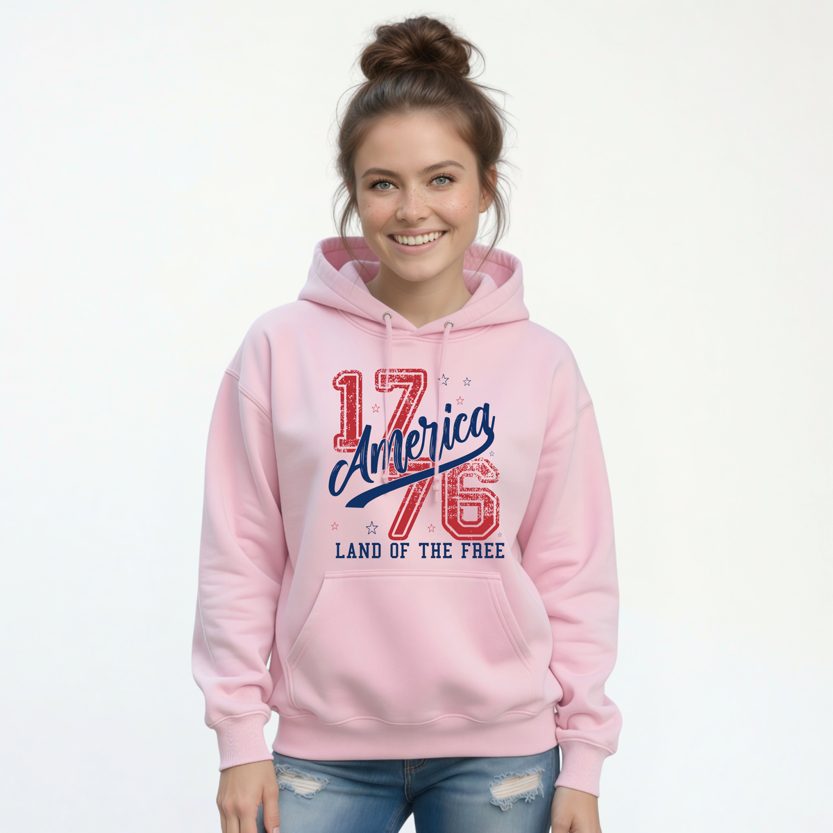 Woman wearing a light pink pullover hoodie with a distressed red and blue America 1776 Land of the Free graphic