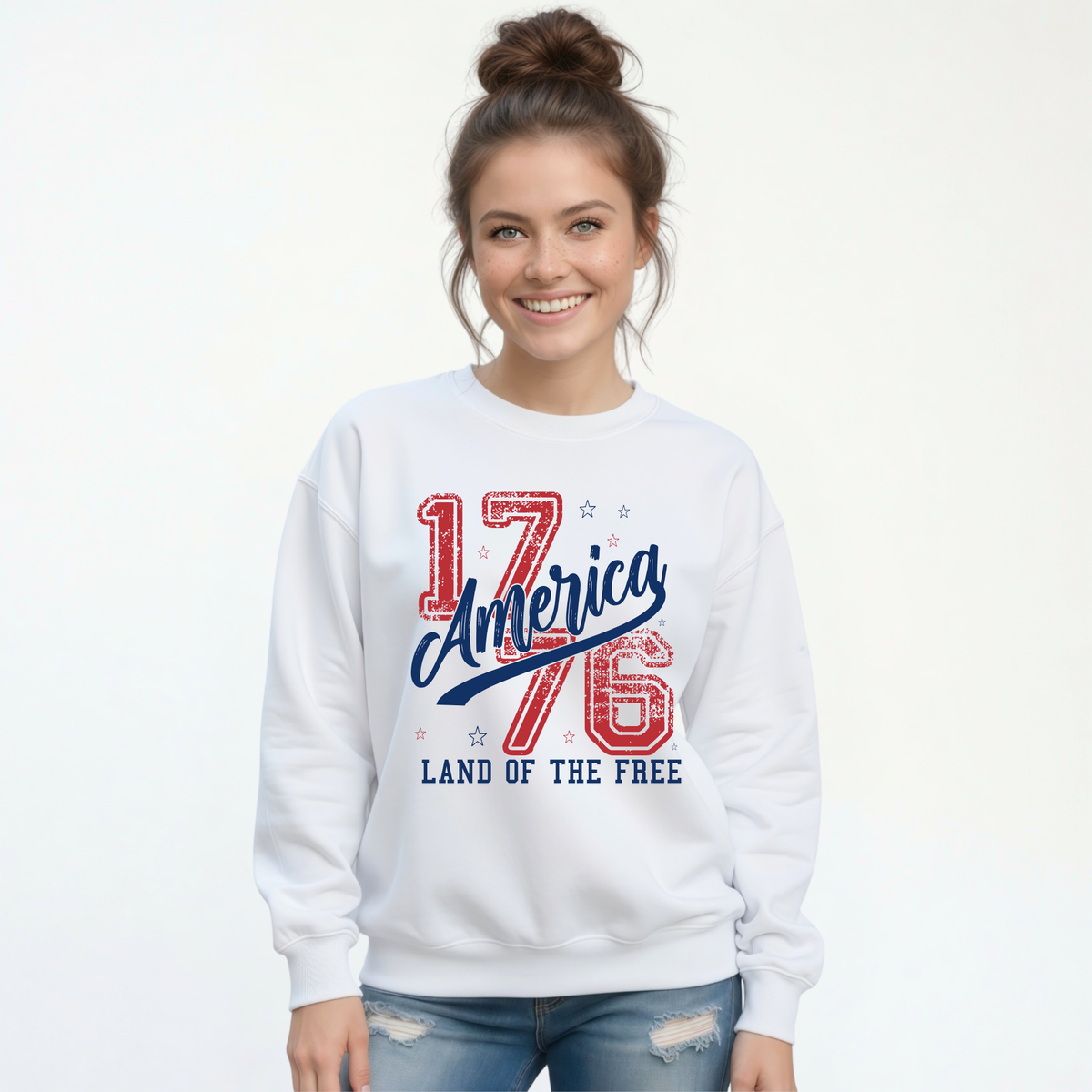 Woman wearing a white crewneck sweatshirt with a distressed red and blue America 1776 Land of the Free graphic