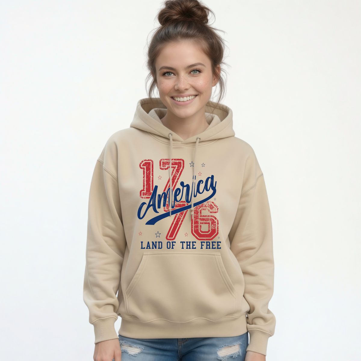 Woman wearing a sand pullover hoodie with a distressed red and blue America 1776 Land of the Free graphic