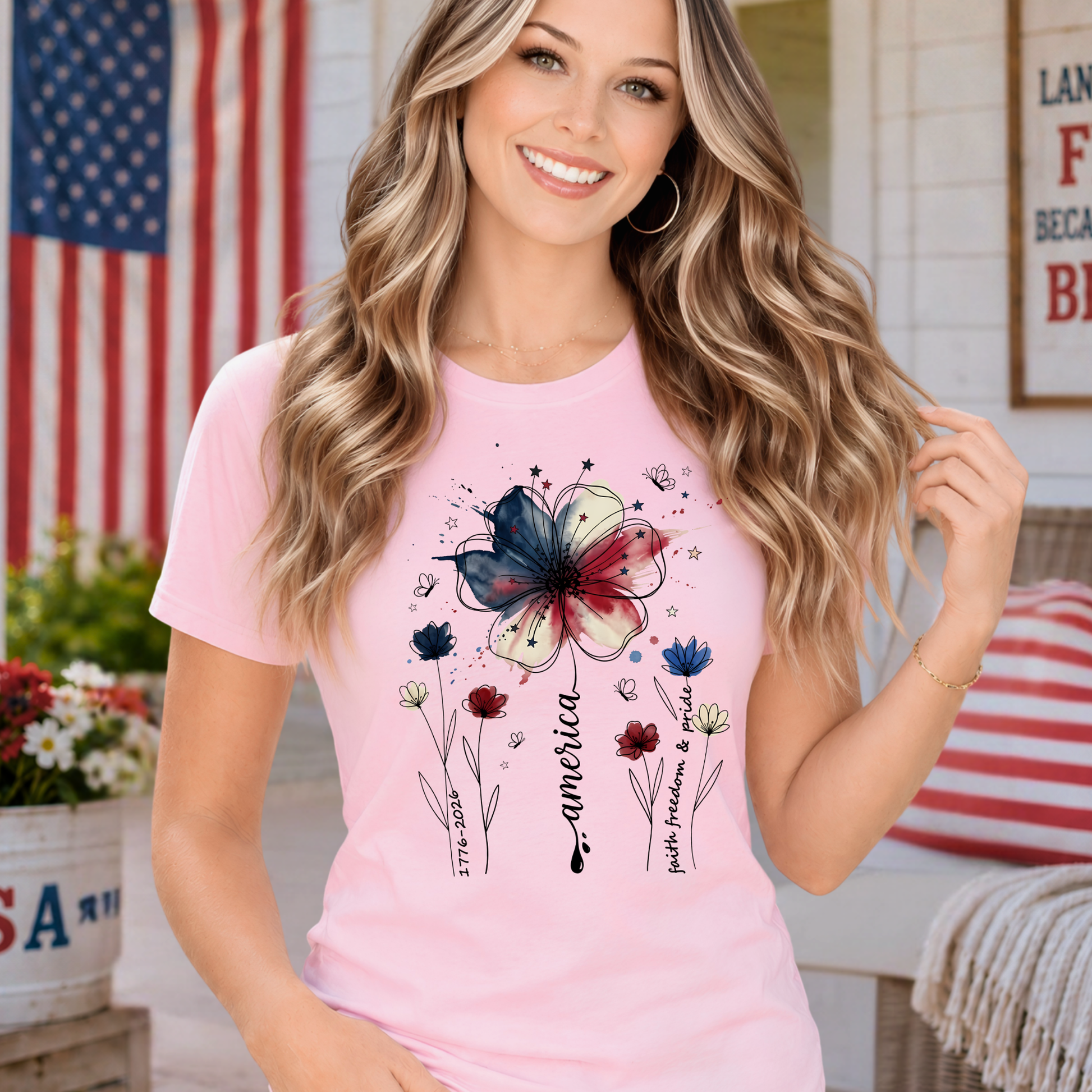 Woman wearing light pink America 250 floral patriotic shirt featuring watercolor red white and blue flower graphic and Faith Family Freedom design.