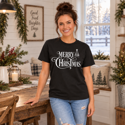 Black Merry Christmas T-shirt modeled in a Christmas dining room, showing the white tree and script design.