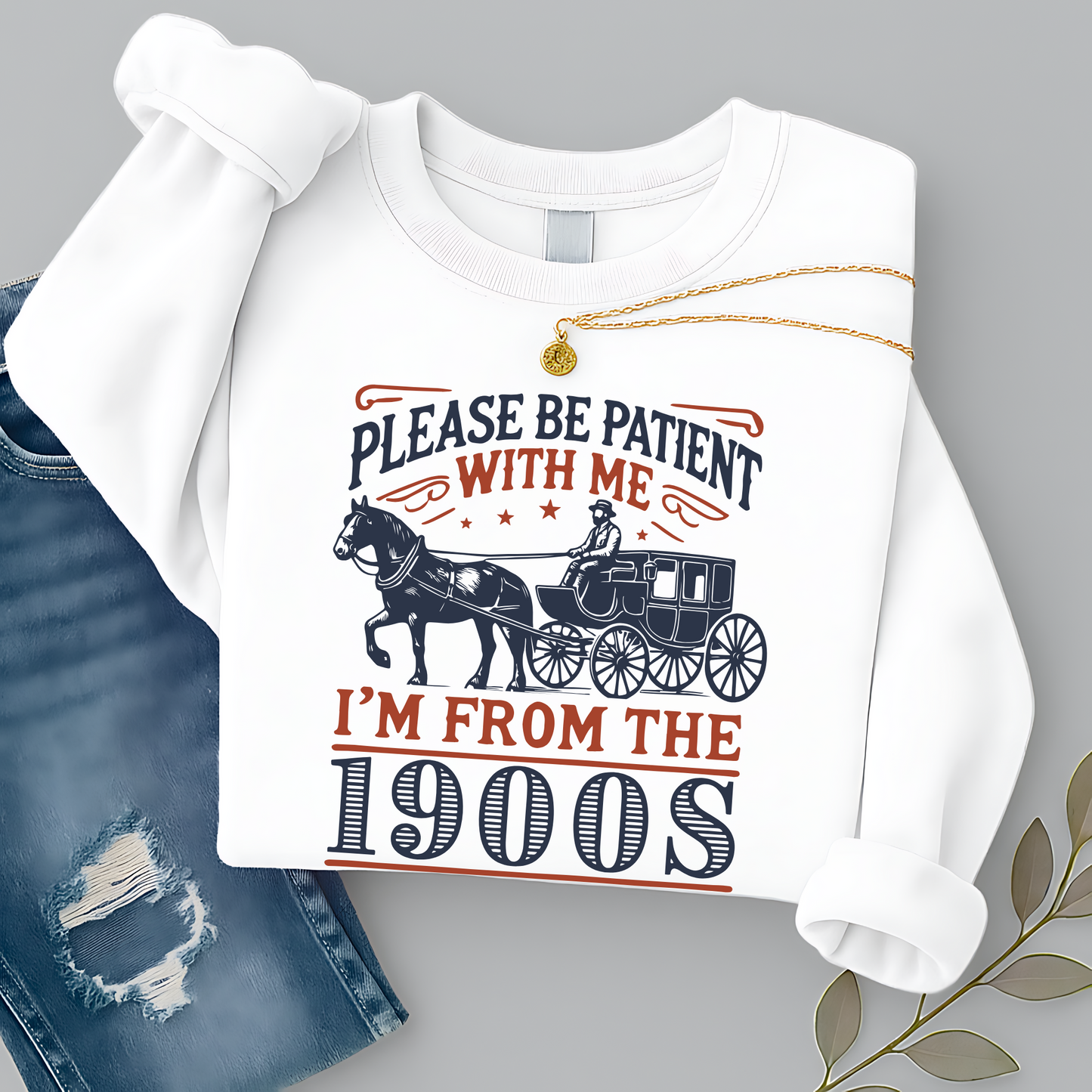 Folded white sweatshirt styled with jeans and necklace flat lay – Please Be Patient With Me I’m From the 1900s graphic sweatshirt for retro gift lovers