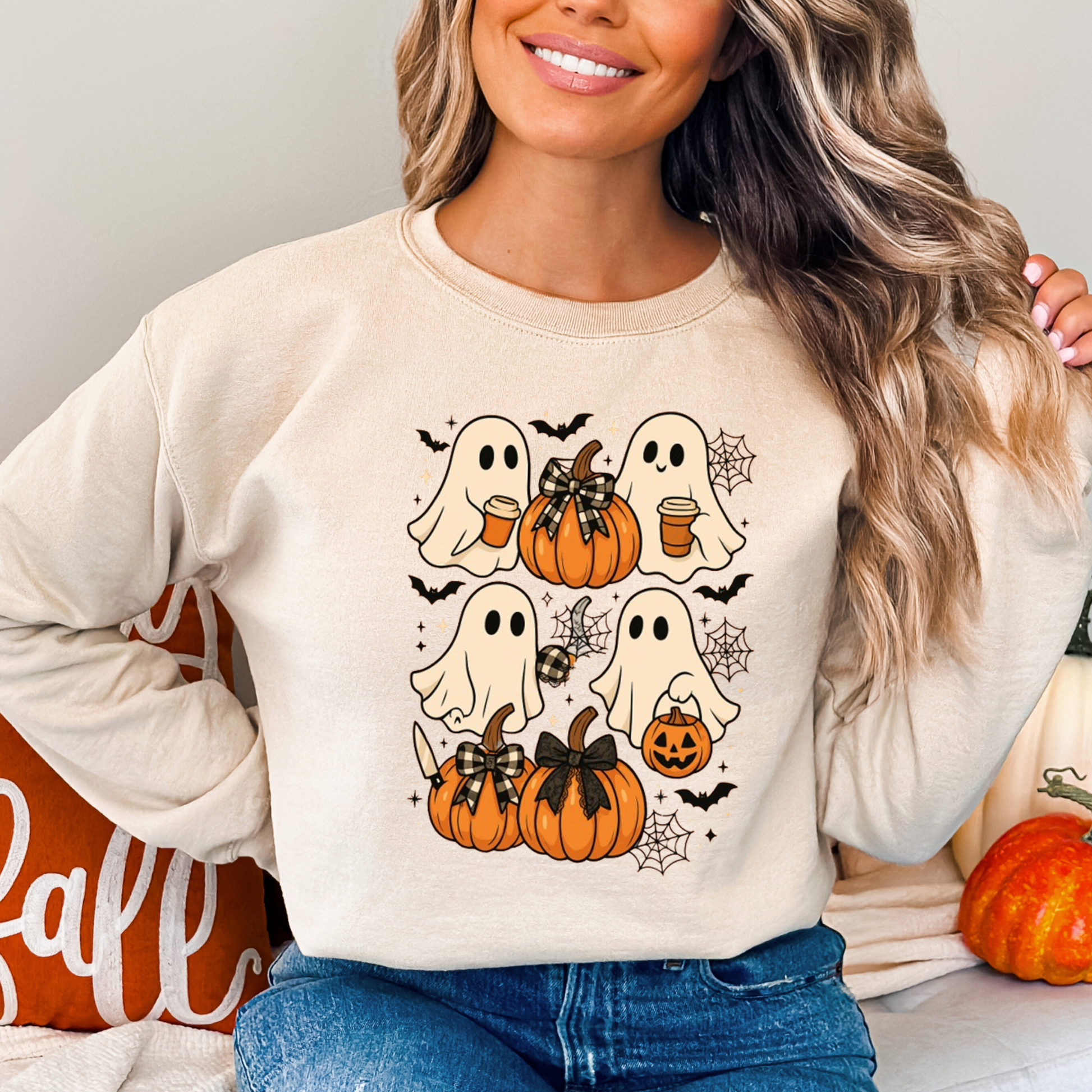Beige Halloween ghost sweatshirt with pumpkins and bats, worn by a woman in cozy fall decor setting. Perfect fall crewneck for Halloween parties and autumn outings.