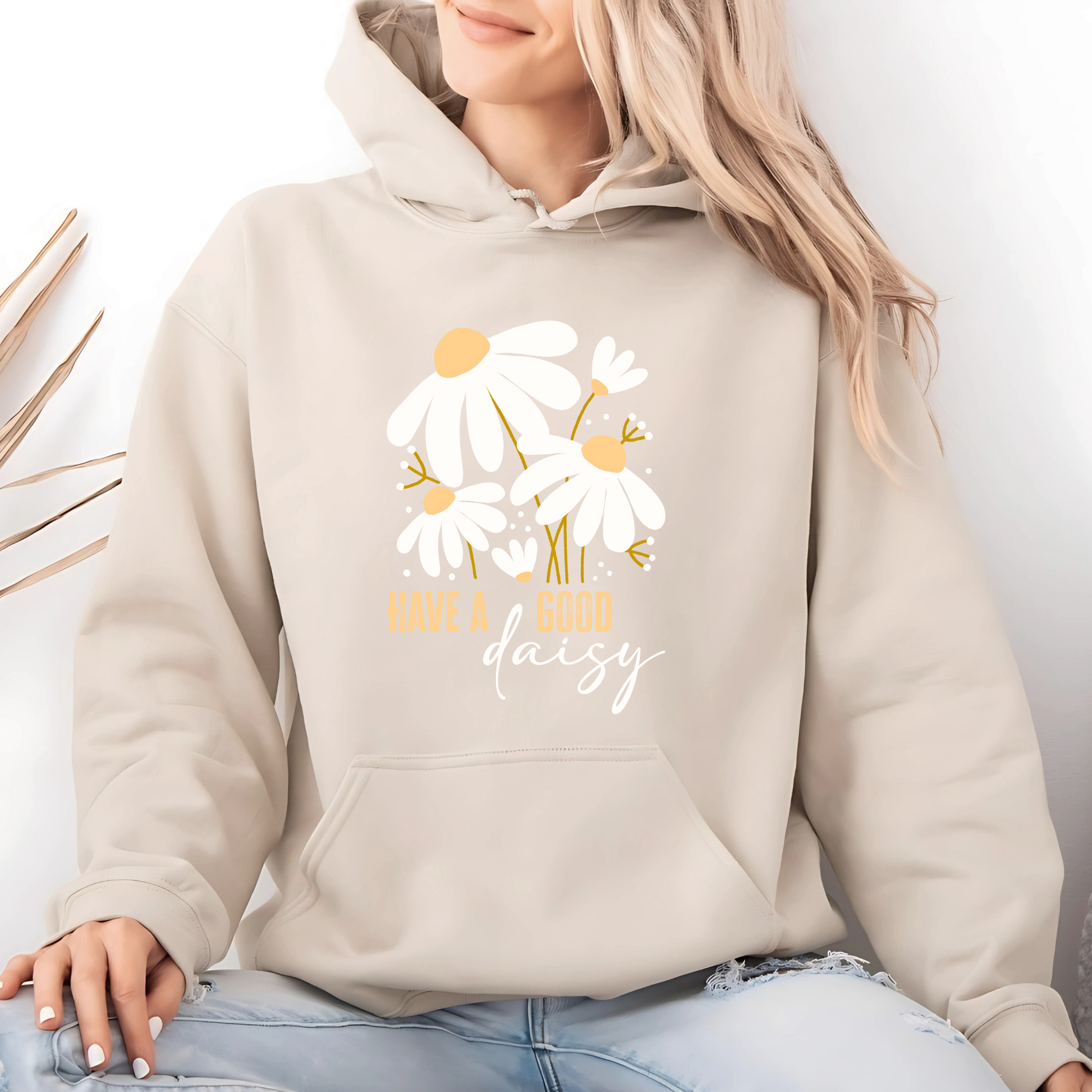 Beige hoodie with floral design and text worn by a person, against a neutral background