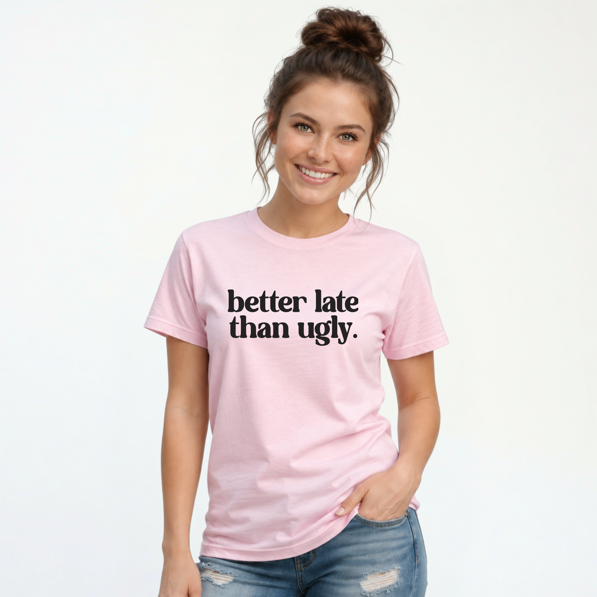 Woman wearing a light pink short-sleeve T-shirt with black Better Late Than Ugly lettering against a white studio background.