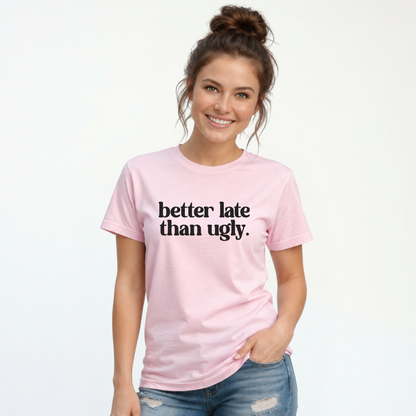 Woman wearing a light pink short-sleeve T-shirt with black Better Late Than Ugly lettering against a white studio background.