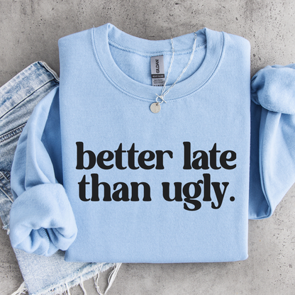 Light blue Better Late Than Ugly crewneck sweatshirt flat lay with black lettering, styled with denim and a necklace.
