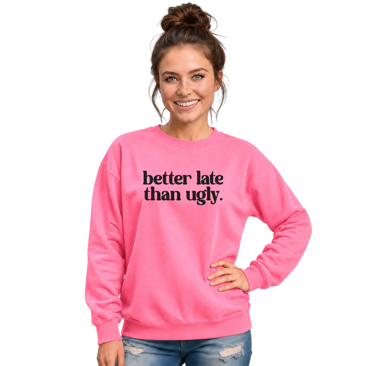 Woman wearing a bright pink crewneck sweatshirt with black Better Late Than Ugly lettering against a white studio background.