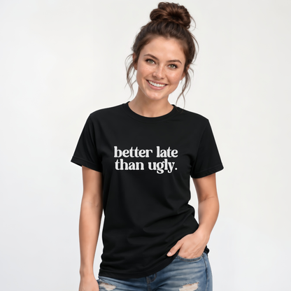 Woman wearing a black short-sleeve T-shirt with white Better Late Than Ugly lettering against a white studio background.