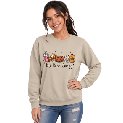 Woman wearing a sand crewneck sweatshirt featuring the Big Back Energy Thanksgiving design with turkey, pie, and fall treats.