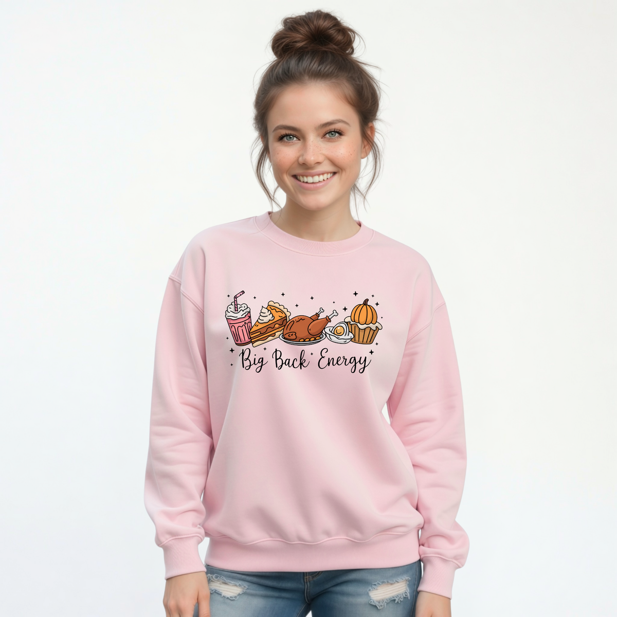 Smiling woman in a light pink crewneck sweatshirt and jeans displays the playful Big Back Energy Thanksgiving design.