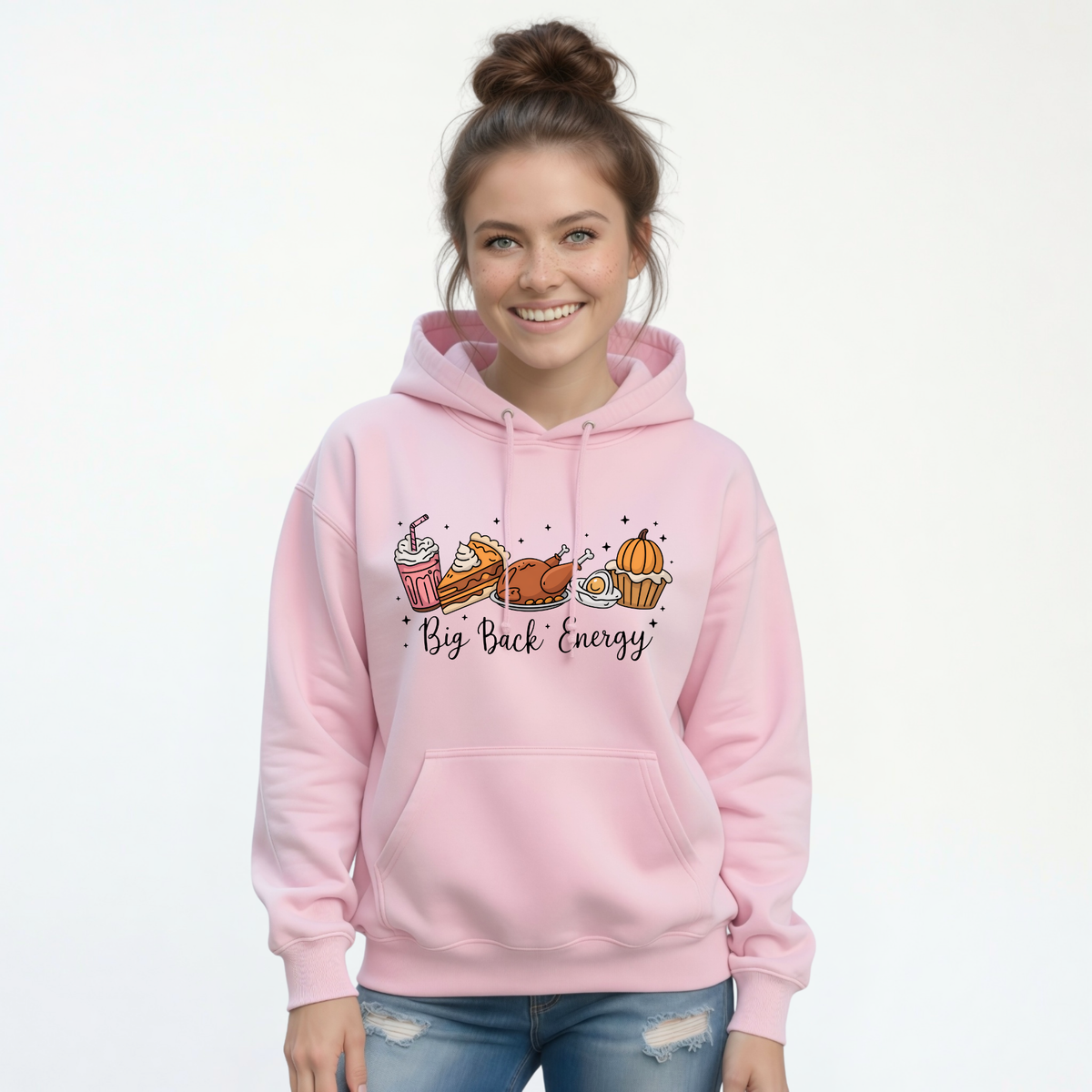 Light pink hoodie modeled by a smiling woman with the Big Back Energy design surrounded by turkey, pie, pumpkin, cookies, and a drink.