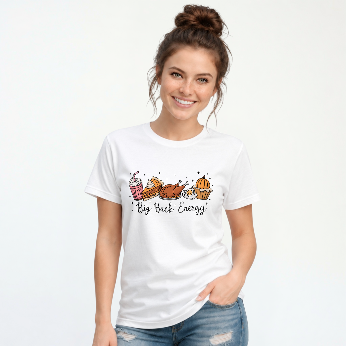 White T-shirt featuring cartoon Thanksgiving foods and Big Back Energy wording, worn by a smiling woman with her hair in a bun.