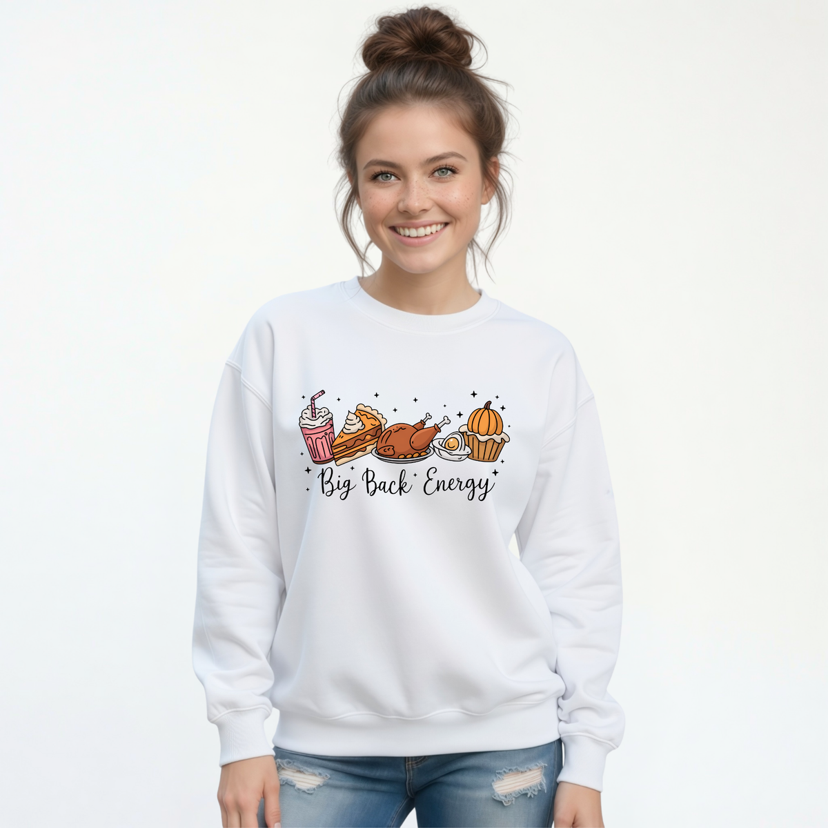 White crewneck sweatshirt with a colorful Big Back Energy Thanksgiving graphic modeled by a smiling woman in blue jeans.