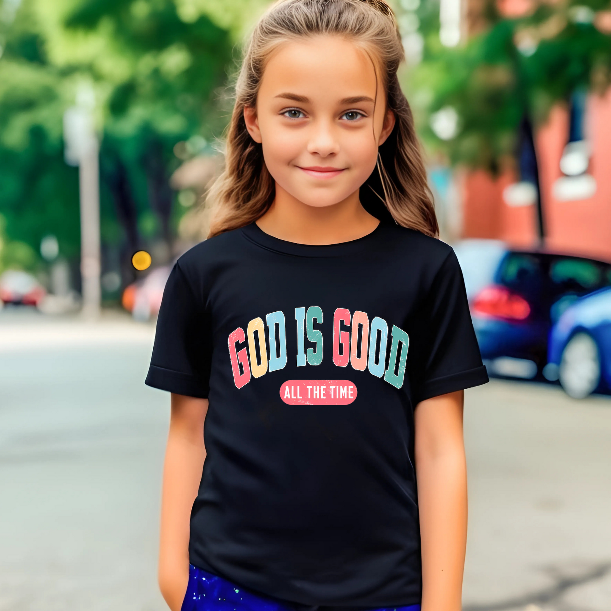 Smiling girl wearing a black T-shirt with the message 'God Is Good All the Time' in colorful text, symbolizing faith and positivity. Perfect for Easter and Christian-themed apparel.
