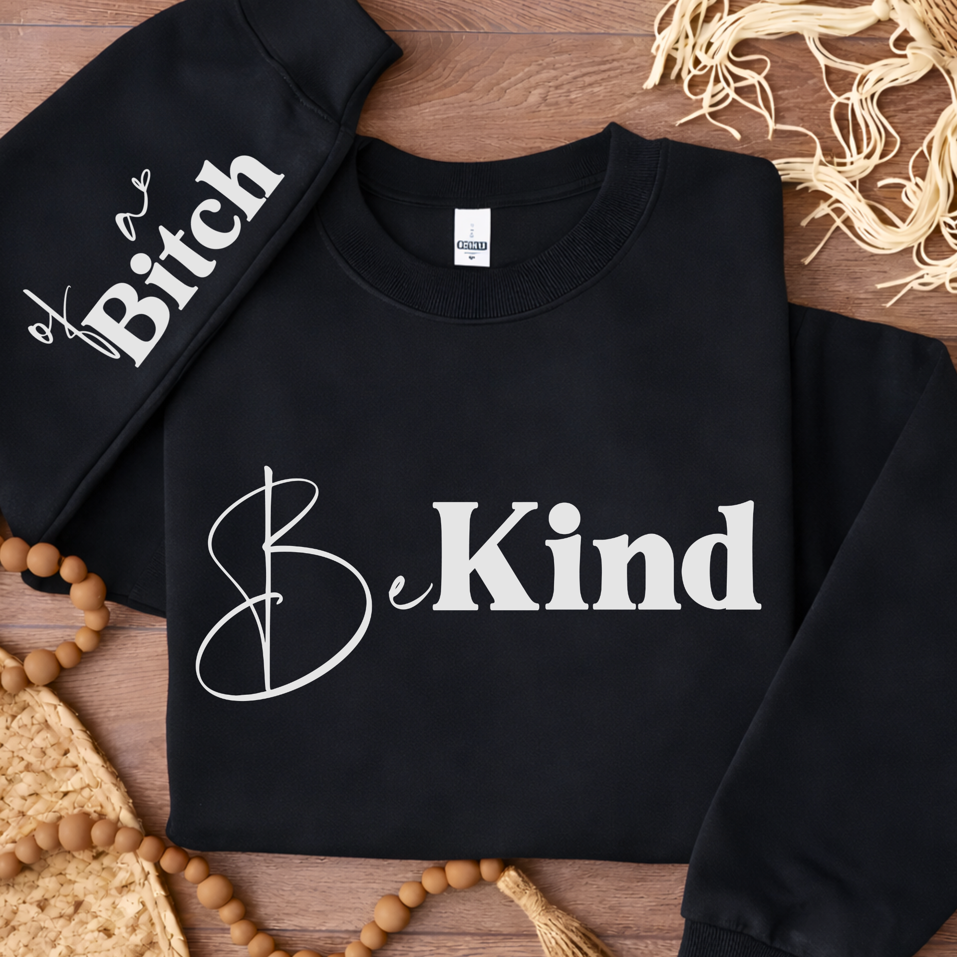 Black sweatshirt with 'Be Kind' text on a wooden surface