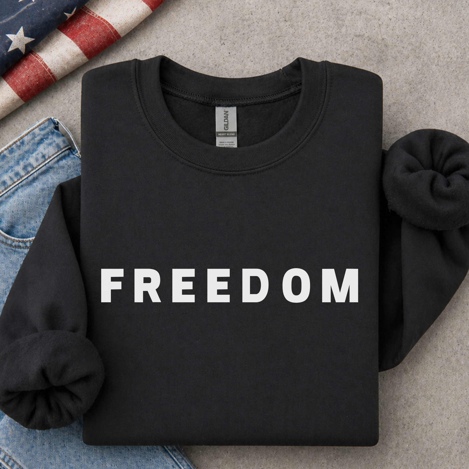 Black sweatshirt with 'FREEDOM' printed on it, placed on a surface with jeans and an American flag.