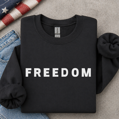 Black sweatshirt with 'FREEDOM' printed on it, placed on a surface with jeans and an American flag.
