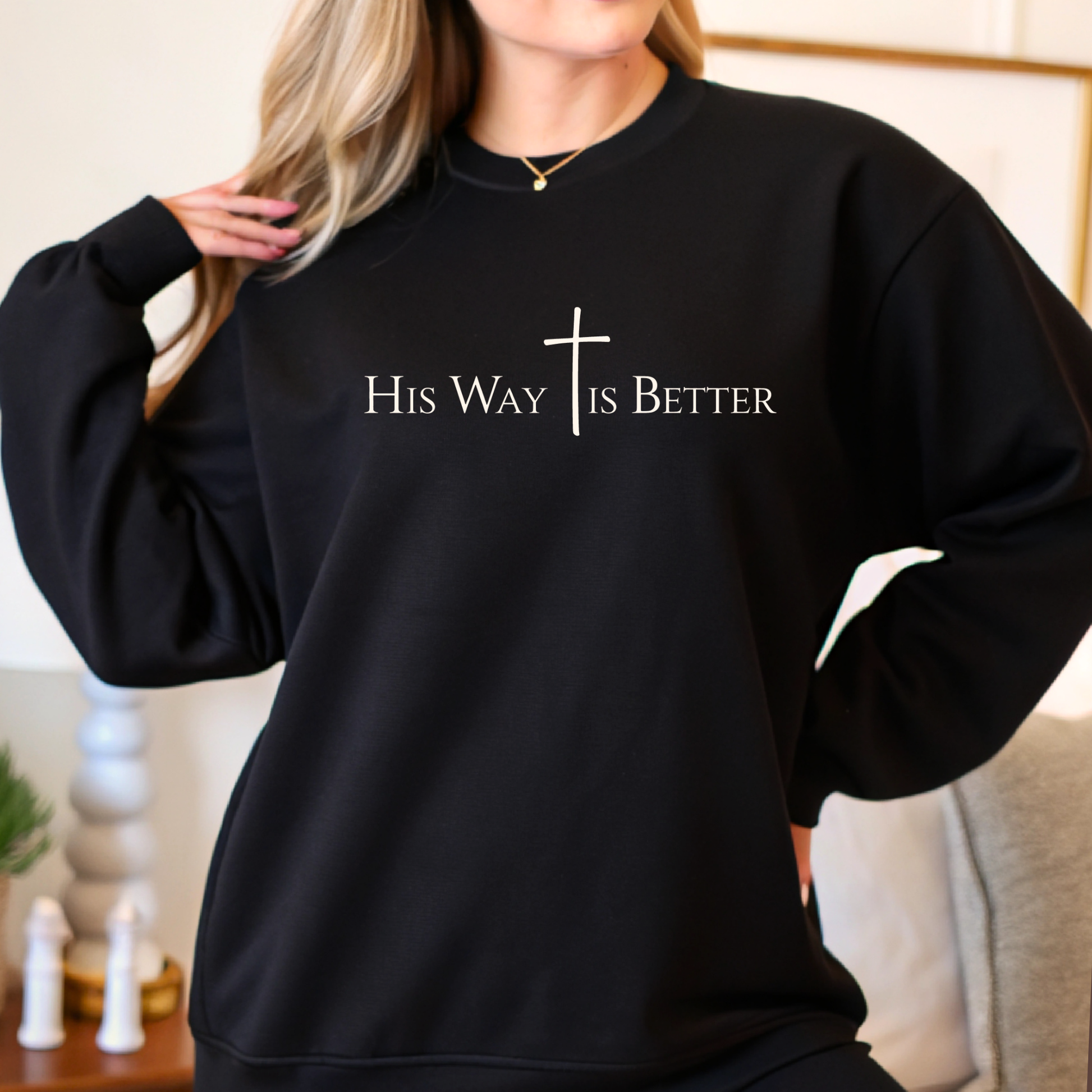 Black sweatshirt with 'His Way is Better' text and cross design worn by a woman indoors.