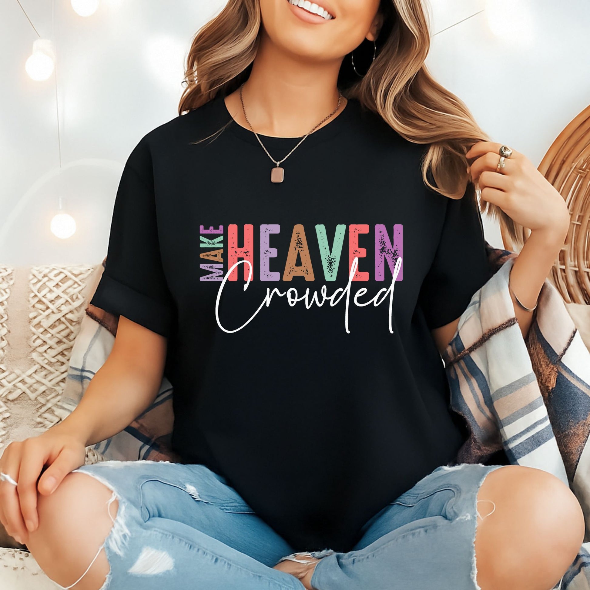 Woman in black Make Heaven Crowded  Christian T-shirt with rolled sleeves sitting in cozy indoor setting