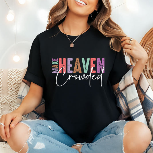 Woman in black Make Heaven Crowded  Christian T-shirt with rolled sleeves sitting in cozy indoor setting