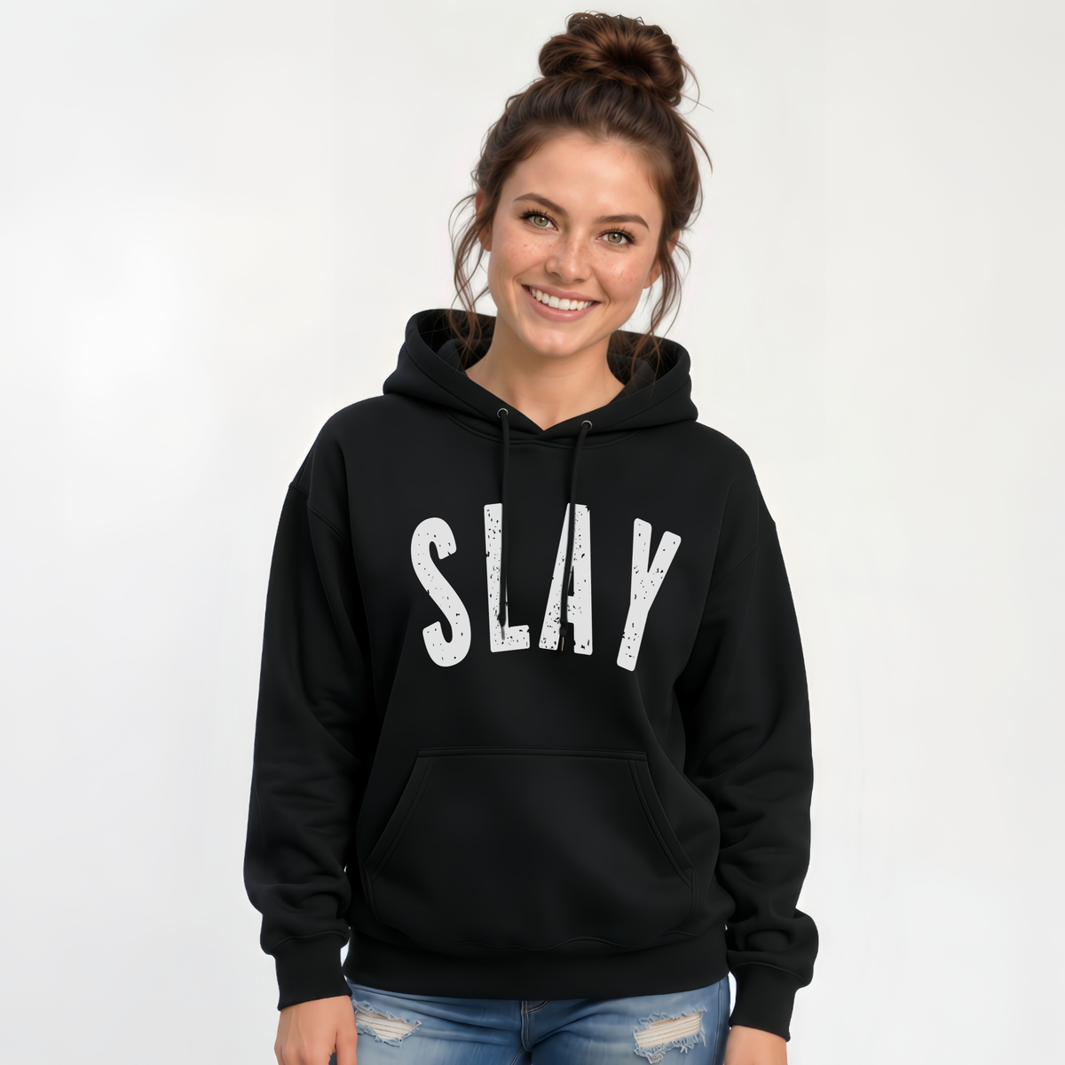 Woman wearing a black SLAY hoodie with bold white distressed lettering against a white studio background.