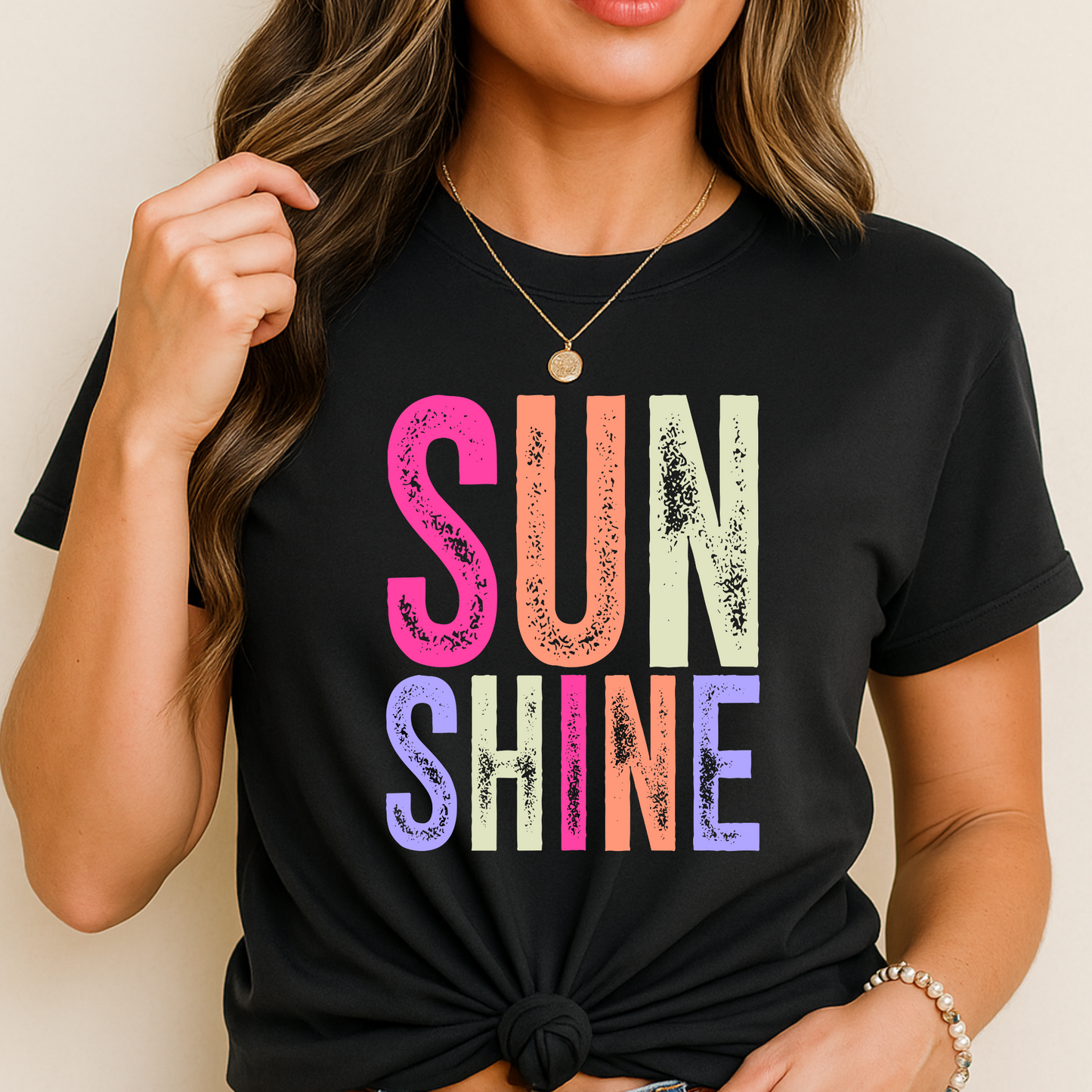 Woman wearing a bright “SUNSHINE” graphic T-shirt in Black, smiling in a relaxed summer setting.