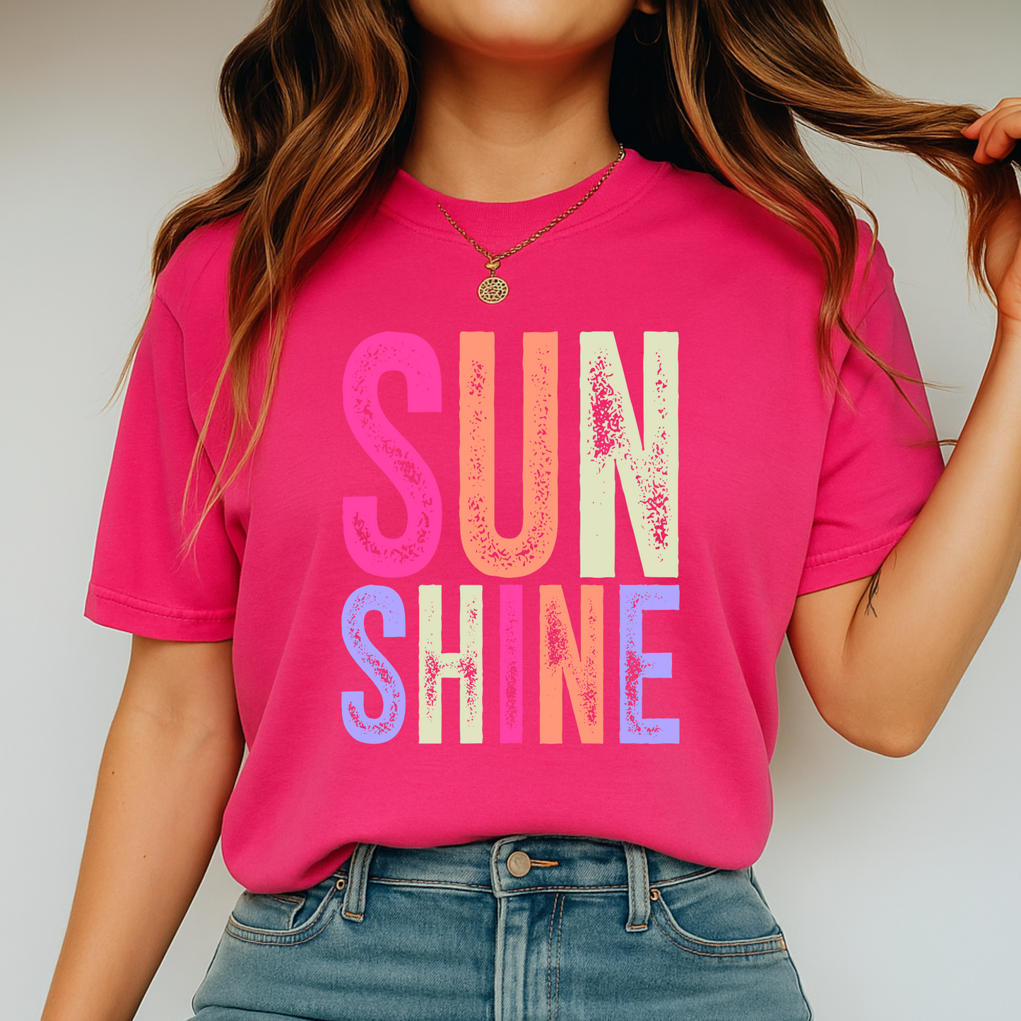 Woman wearing a bright “SUNSHINE” graphic T-shirt in dark pink, smiling in a relaxed summer setting.