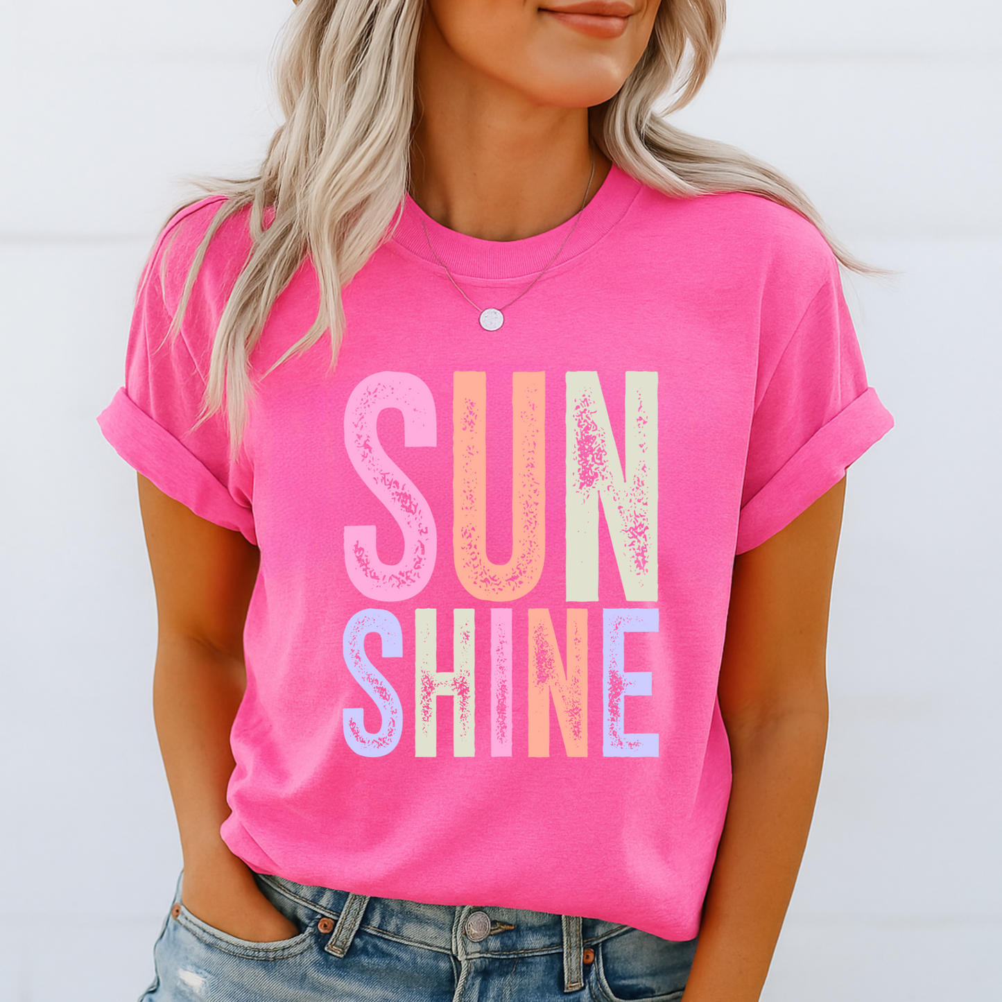 Woman wearing a bright “SUNSHINE” graphic T-shirt in Bright Pink, smiling in a relaxed summer setting.