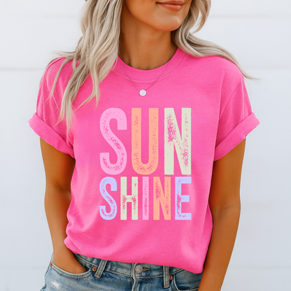 Woman wearing a bright “SUNSHINE” graphic T-shirt in Bright Pink, smiling in a relaxed summer setting.