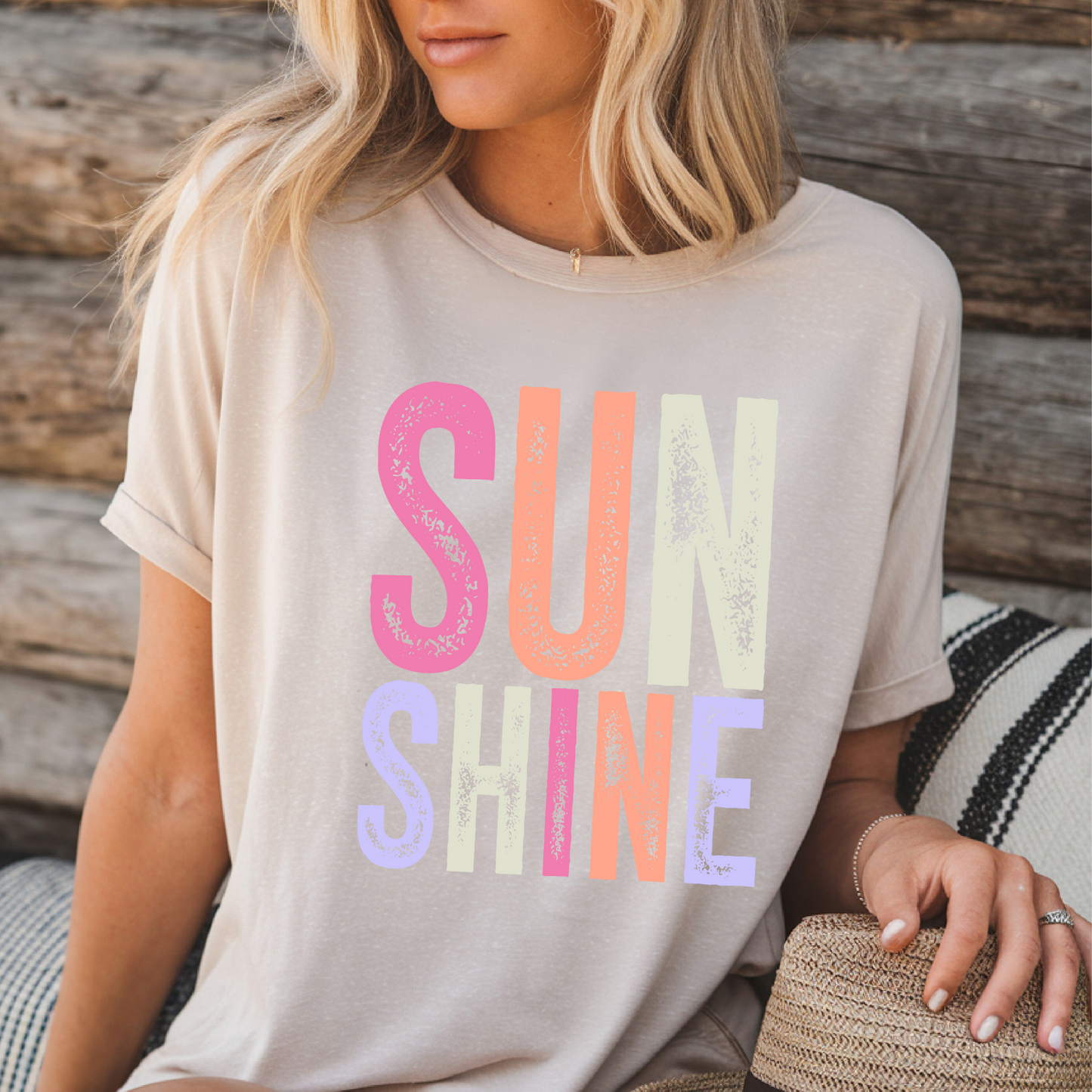 Woman wearing a bright “SUNSHINE” graphic T-shirt in Sand, smiling in a relaxed summer setting.