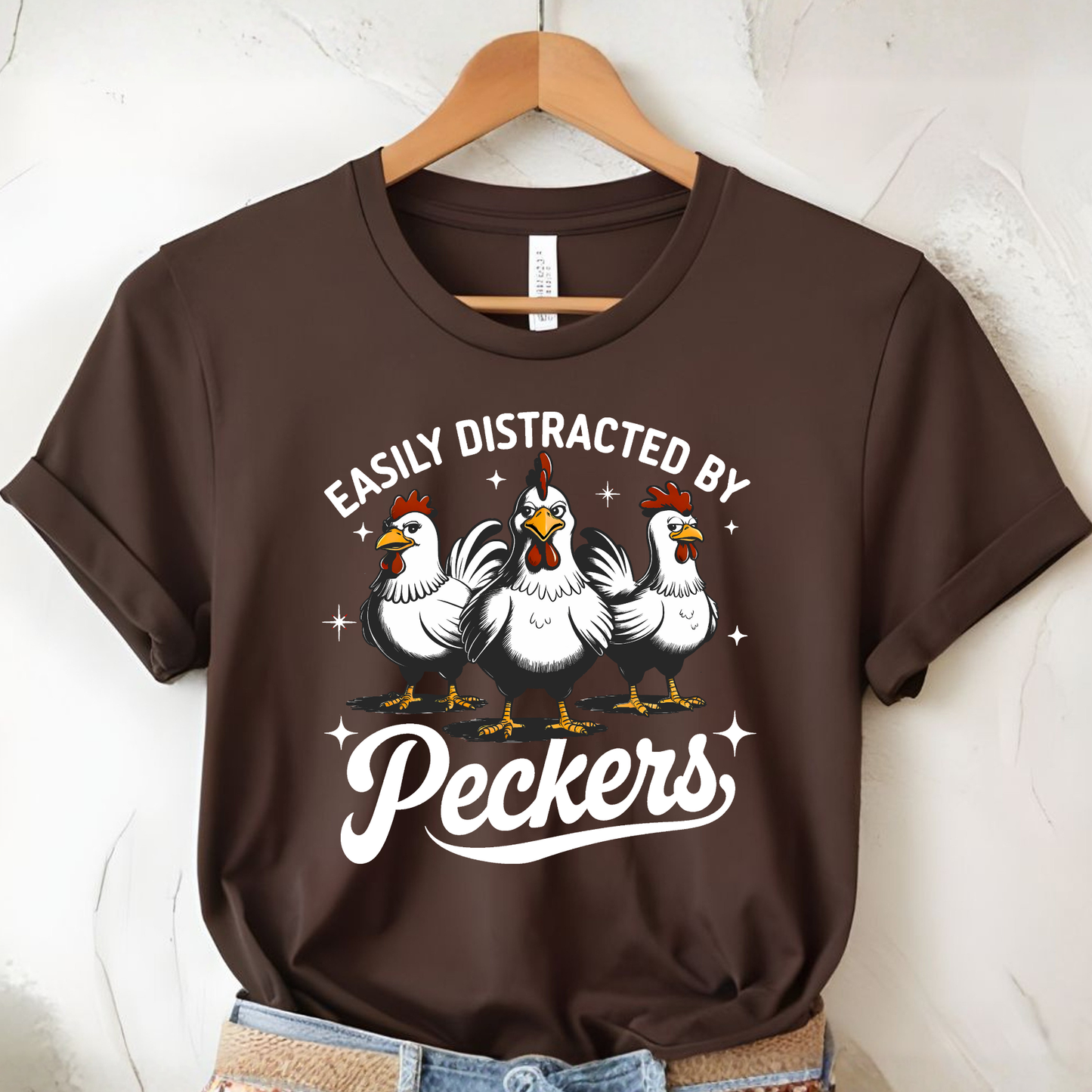 Brown t-shirt with chicken graphic and text on a hanger against a white wall.