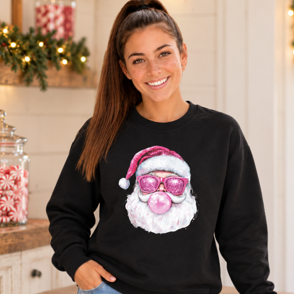 Woman wearing a black Bubblegum Santa crewneck sweatshirt in a simple Christmas kitchen with peppermint candy jars and greenery