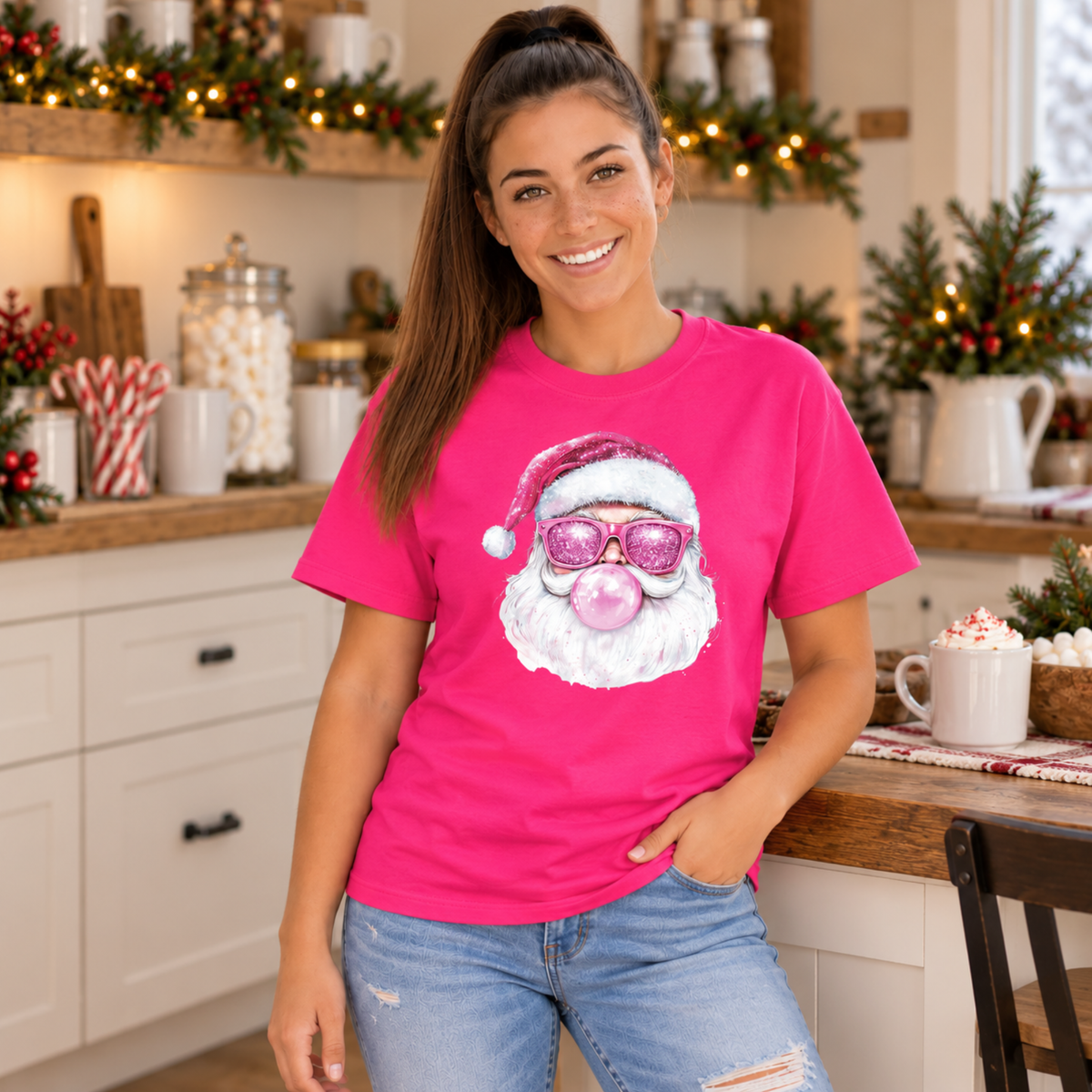 Woman wearing a bright pink Bubblegum Santa T-shirt in a cozy Christmas kitchen with hot cocoa and candy canes