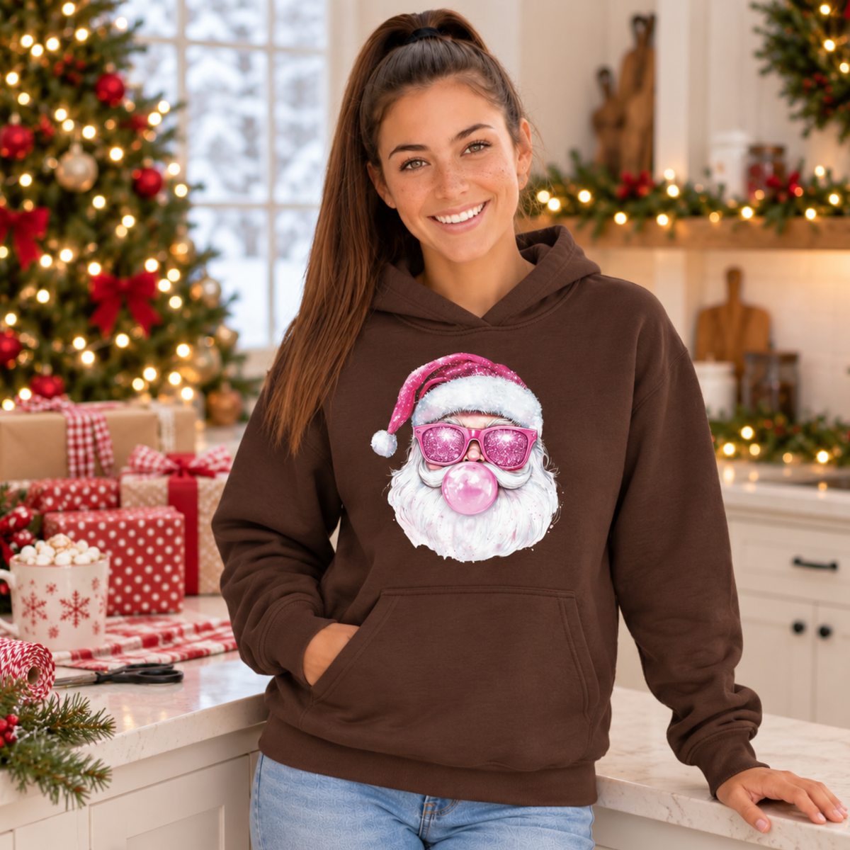 Woman wearing a brown Bubblegum Santa hoodie beside wrapped gifts in a cozy Christmas kitchen