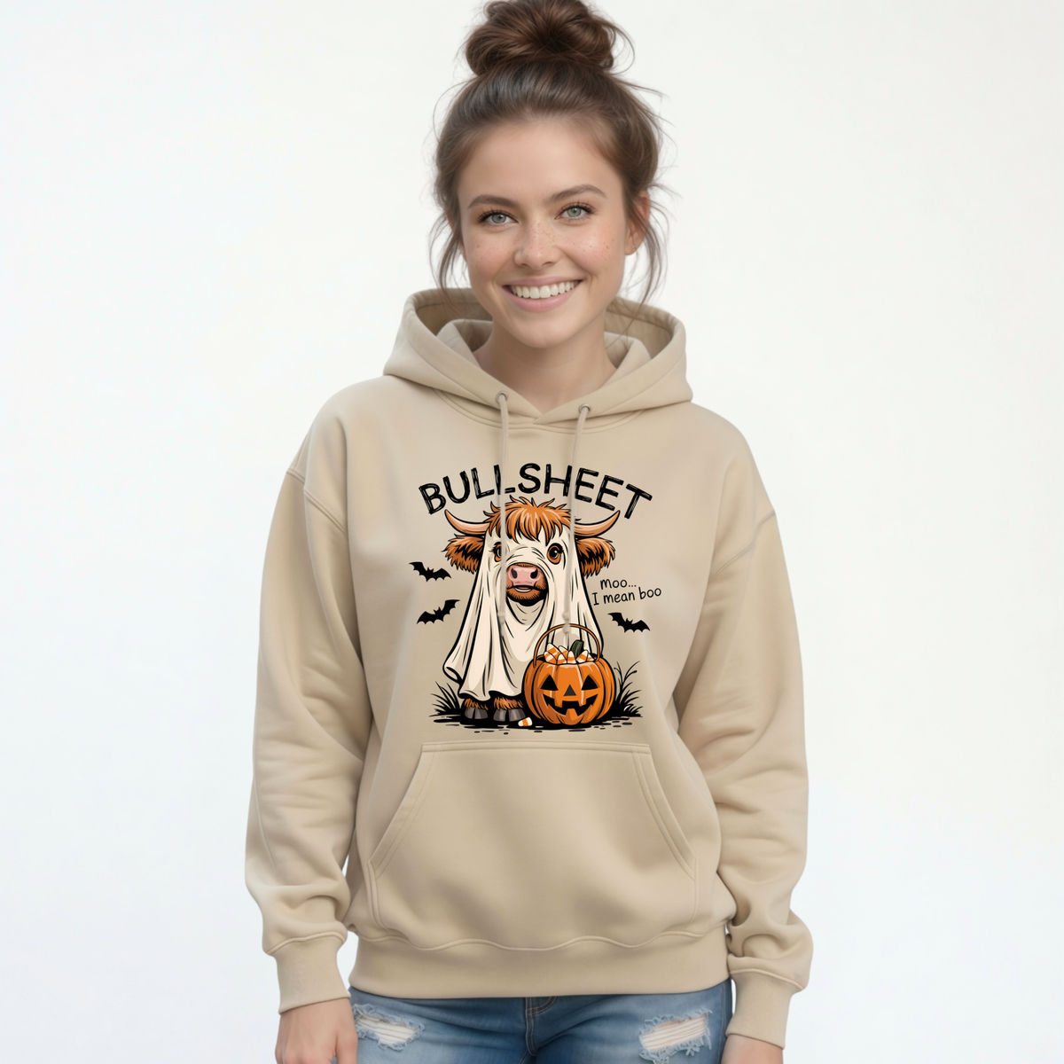 Woman wearing a Sand pullover hoodie with the Bullsheet Halloween Highland cow ghost and jack-o'-lantern design.