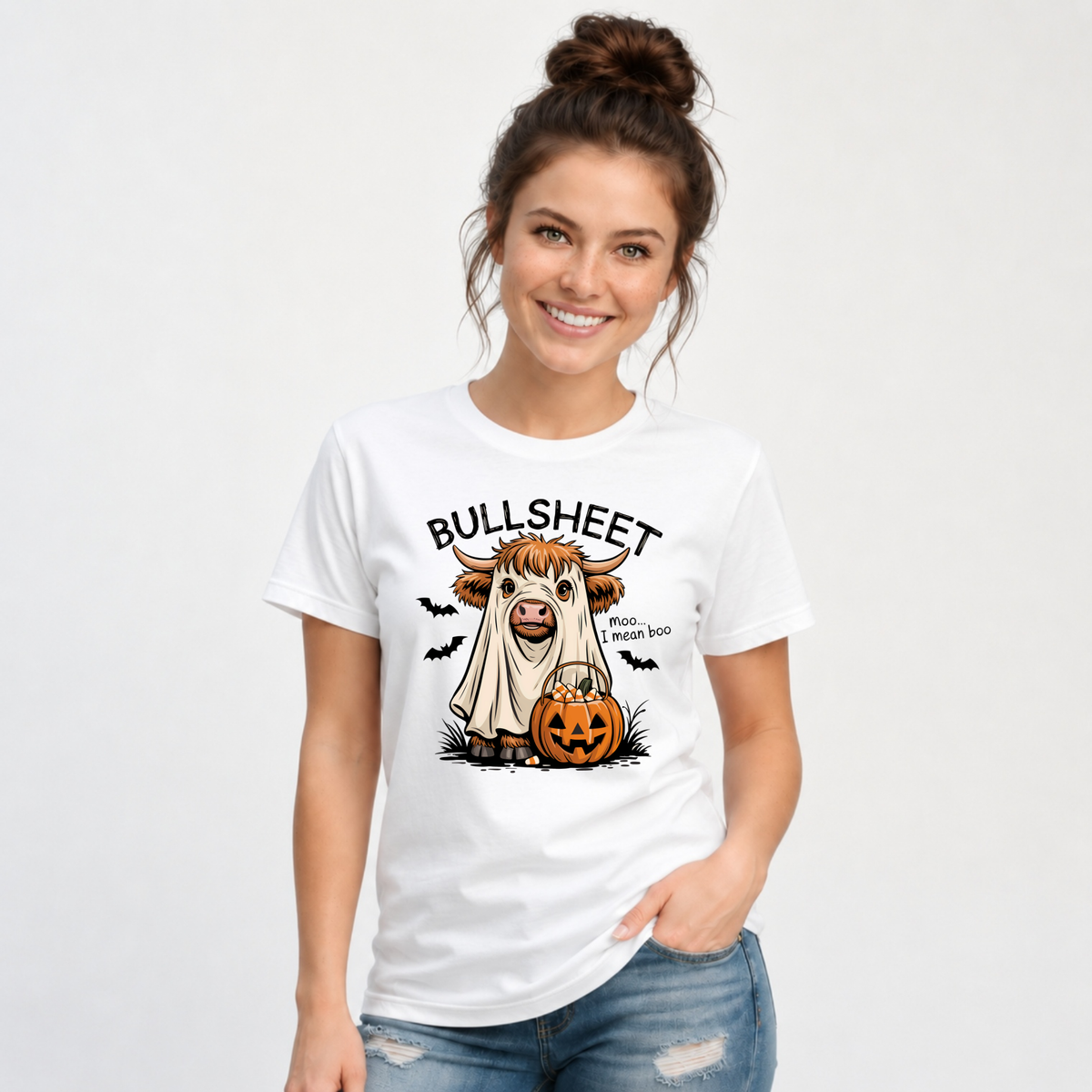Woman wearing a White T-shirt with the Bullsheet Halloween Highland cow ghost and jack-o'-lantern design.