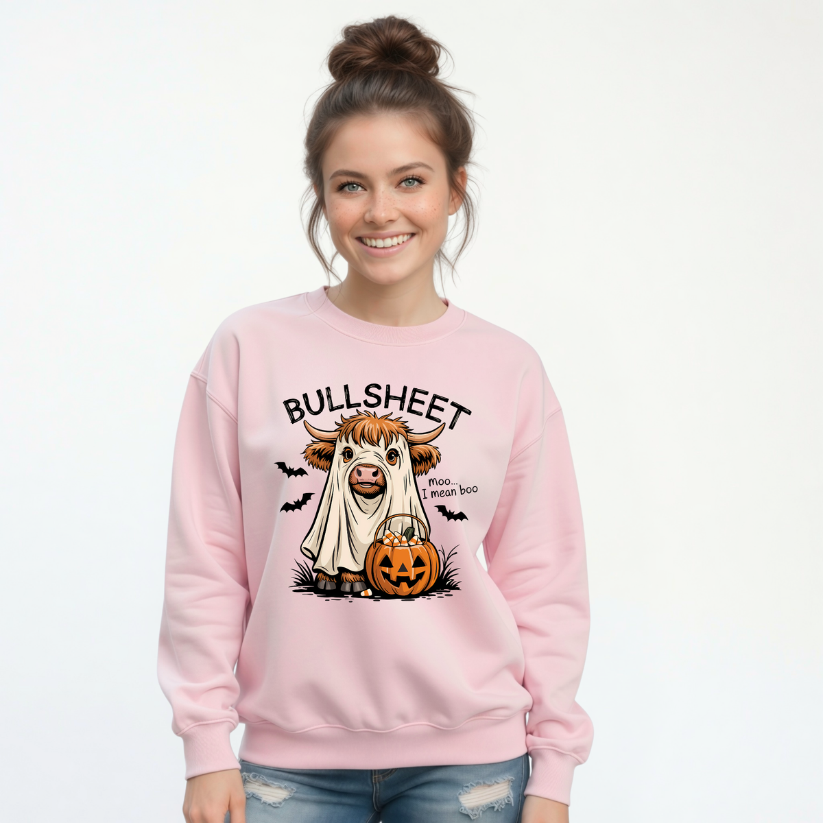 Woman wearing a Light Pink crewneck sweatshirt with the Bullsheet Halloween Highland cow ghost and jack-o'-lantern design.