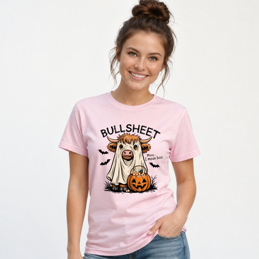 Woman wearing a Light Pink T-shirt with the Bullsheet Halloween Highland cow ghost and jack-o'-lantern design against a white background.